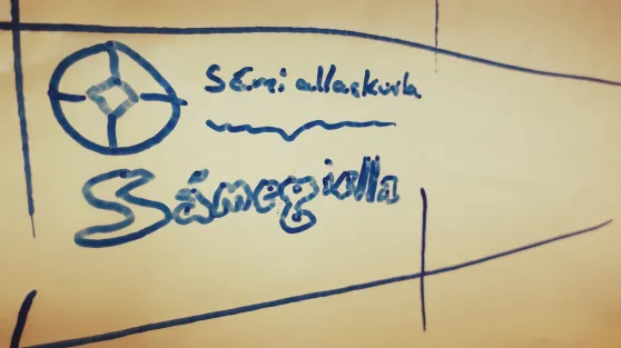 Govva whiteboard tavvalis mas sárgojuvvon Sámi allaskuvla namma, logo ja sátni Sámegiella.