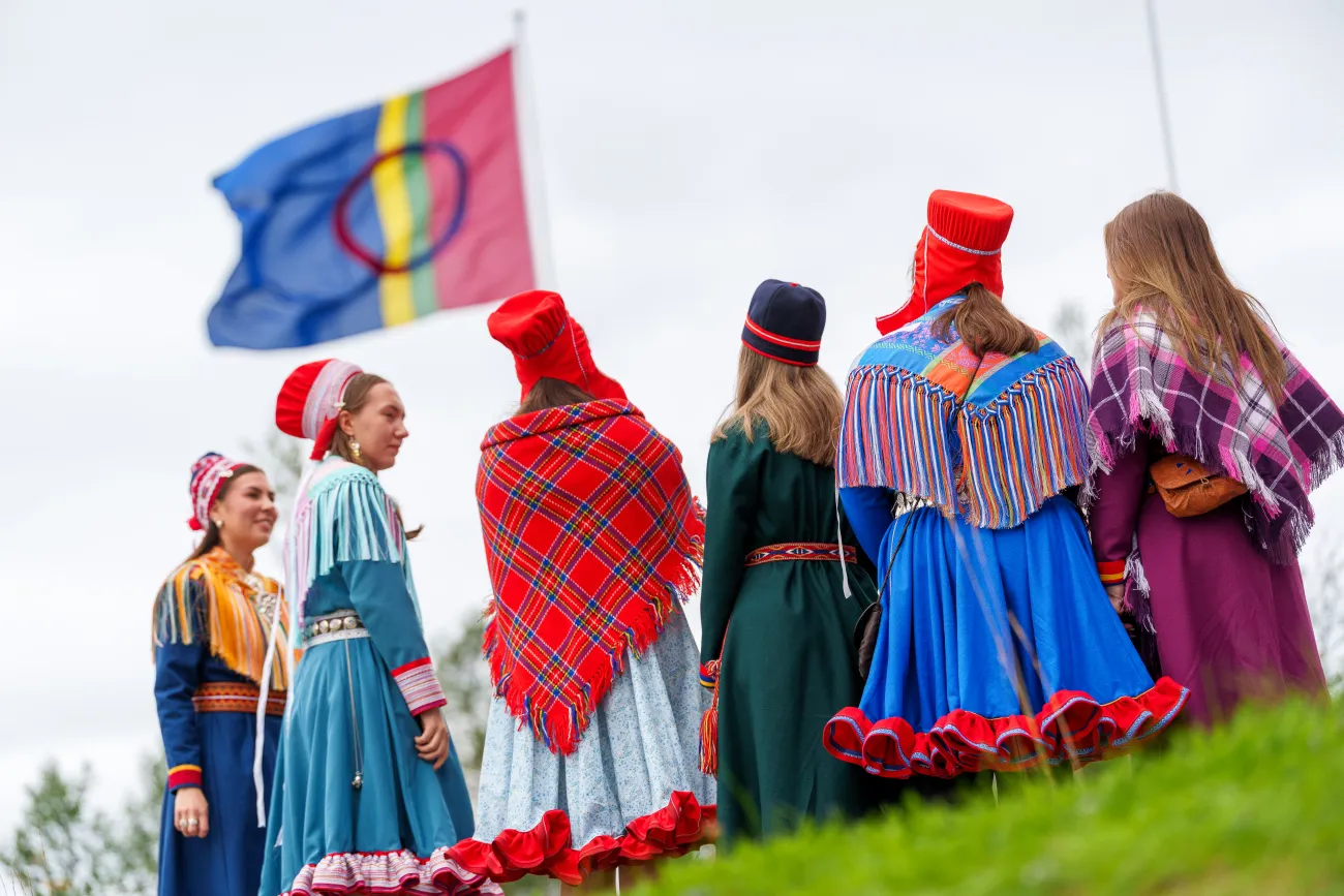 Koftekledde studenter står med ryggen vendt mot kamera. Samisk flagg i bakgrunnen.