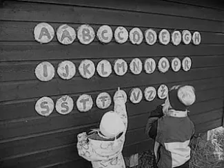 2 children pointing at letters hung up on a wall