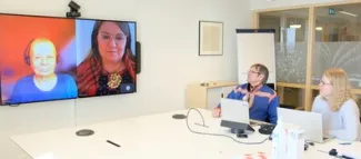 2 people at a conference table having a video call with 2 people on a screen