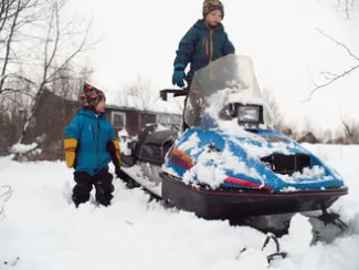 picture of a snowmobile with an older child on it and a younger one next to it
