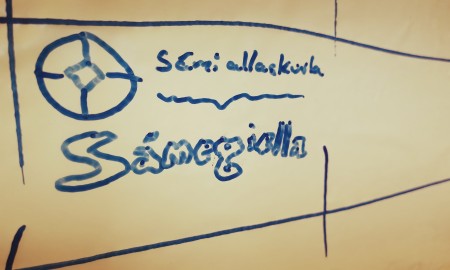 Govva whiteboard tavvalis mas sárgojuvvon Sámi allaskuvla namma, logo ja sátni Sámegiella.